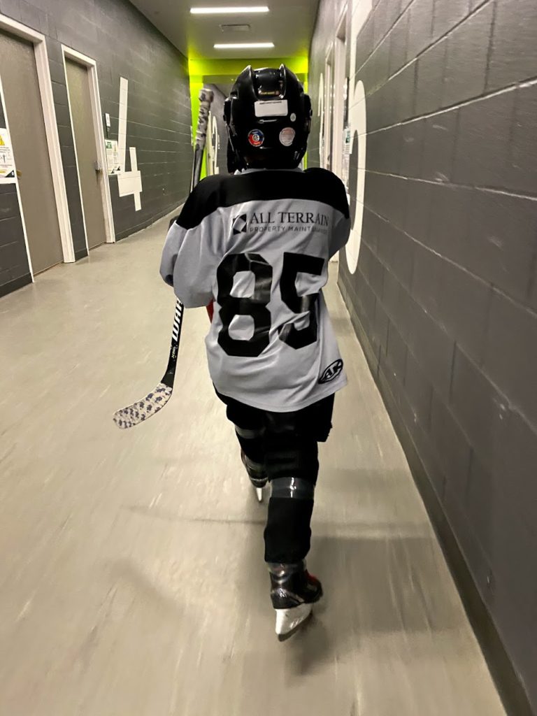A child in hockey equipment walking through a hallway.